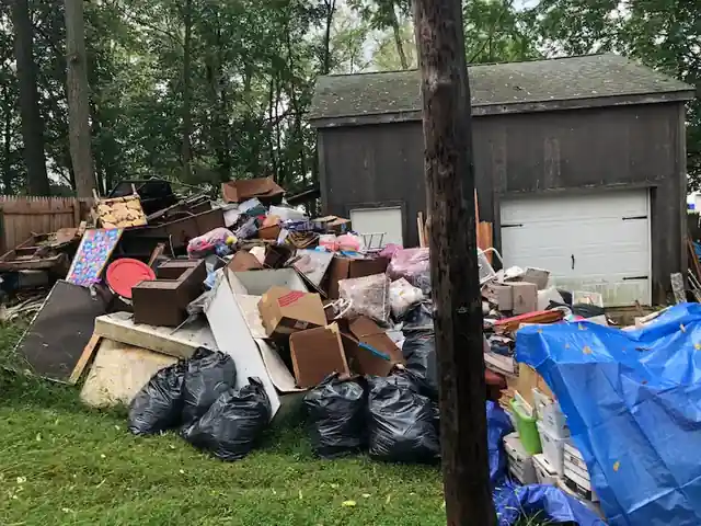 Bags, furniture and tarps piled on the grass in front of a two-door barn shed