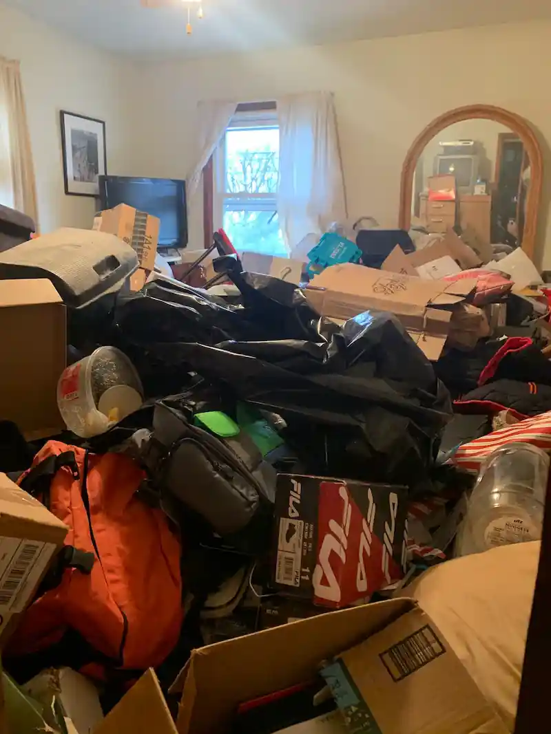 Morristown bedroom piled high with bags, clothing and boxes