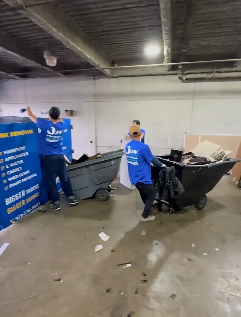 Two JunkDoctors crew members in blue uniforms wheeling a loaded cart out of a basement