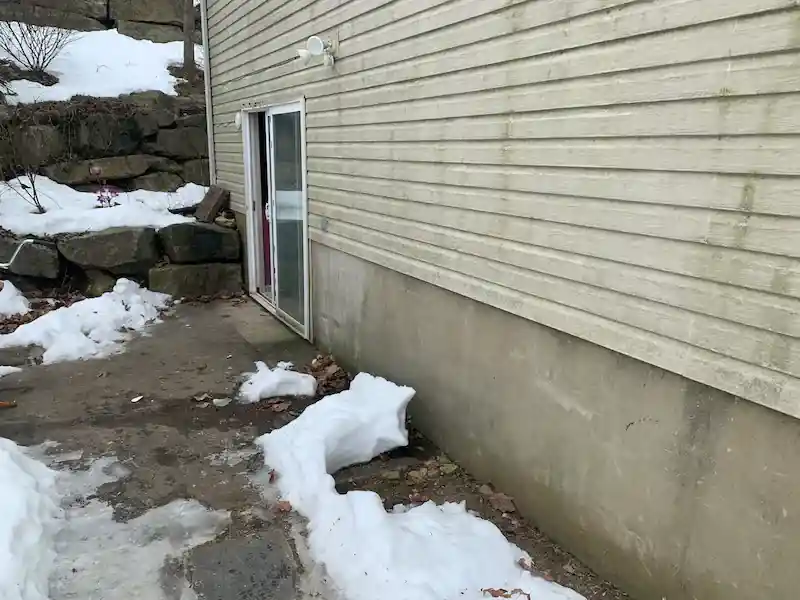 The same snowy side yard with the bags gone and the path to the door open