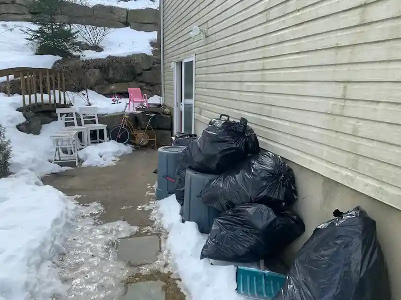 Black contractor bags and broken patio chairs along a snowy side yard